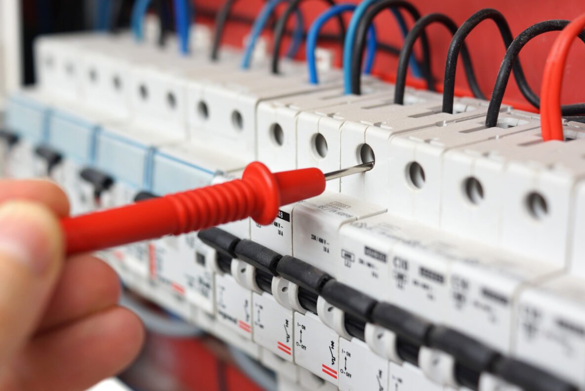 Hand of an electrician with multimeter probe at an electrical sw